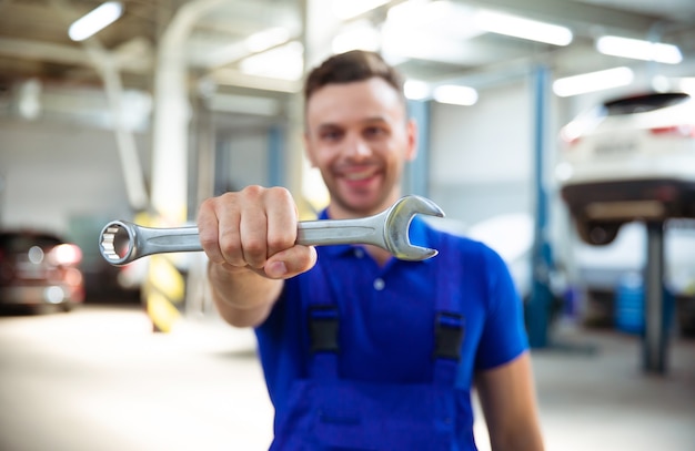 Cerrar foto de feliz mecánica automotriz con una llave de boca en mano en el fondo de la reparación de un automóvil