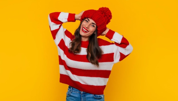 Cerrar foto de una hermosa mujer morena feliz con sombrero rojo de invierno y bufanda y posando aislado sobre fondo amarillo