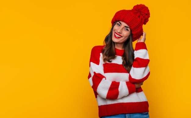 Cerrar foto de una hermosa mujer morena feliz con sombrero rojo de invierno y bufanda y posando aislado sobre fondo amarillo