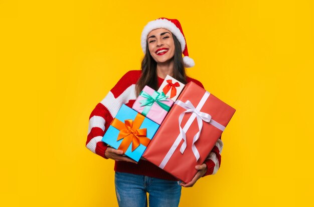 Cerrar foto de hermosa mujer sonriente emocionada con muchas cajas de regalo de Navidad en las manos mientras se divierte y posa sobre fondo amarillo