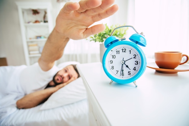 Cerrar foto de hombre barbudo joven guapo acostado en la cama y relajarse en la mañana