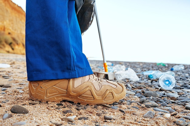 Cerrar foto de un hombre recogiendo basura con una herramienta de agarre en la playa