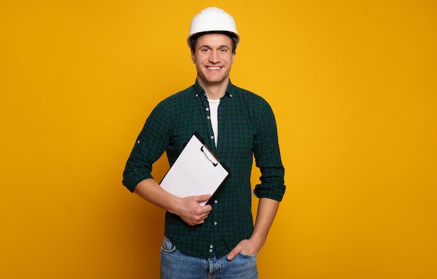 Cerrar una foto de joven capataz o arquitecto feliz y confiado en construir casco está planteando aislado sobre fondo amarillo.