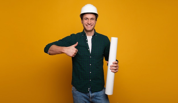 Cerrar una foto de joven capataz o arquitecto feliz y confiado en construir casco está planteando aislado sobre fondo amarillo.