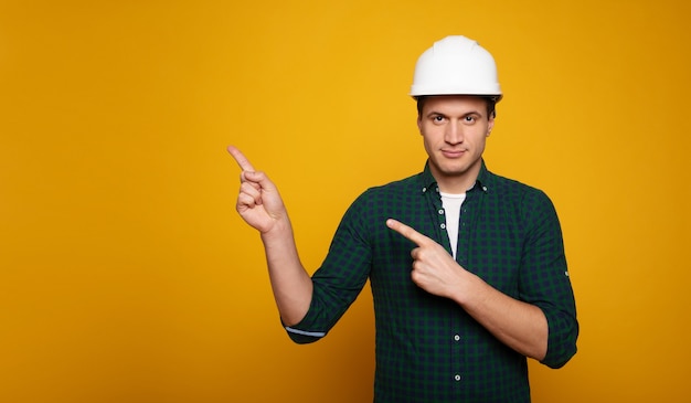 Cerrar una foto de joven capataz o arquitecto feliz y confiado en construir casco está planteando aislado sobre fondo amarillo.