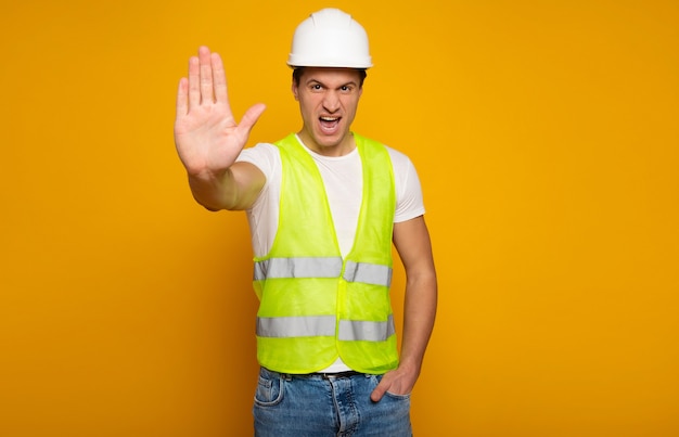 Cerrar una foto de joven capataz o arquitecto feliz y confiado en construir casco está planteando aislado sobre fondo amarillo.