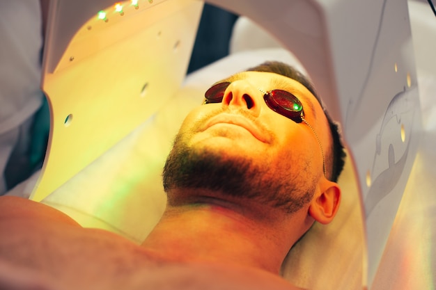 Foto cerrar foto de un joven positivo que parece feliz y sonriente mientras está en el moderno solarium