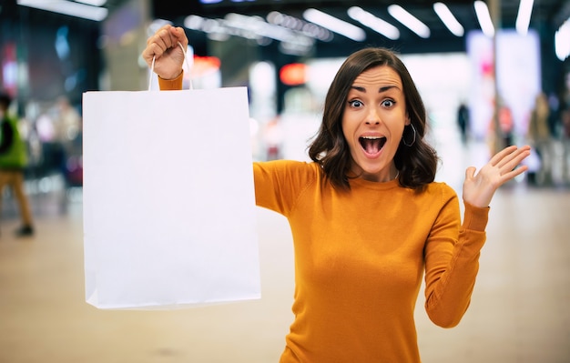 Foto cerrar una foto de una linda mujer joven está mostrando una bolsa blanca en el centro comercial