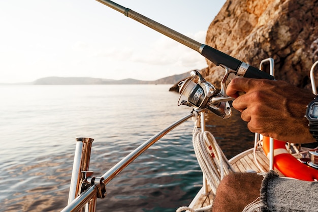 Cerrar foto de manos masculinas sosteniendo la caña de pescar mientras se pesca en velero en mar abierto