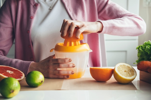 Cerrar foto de una mujer haciendo jugo de frutas en casa con un exprimidor manual