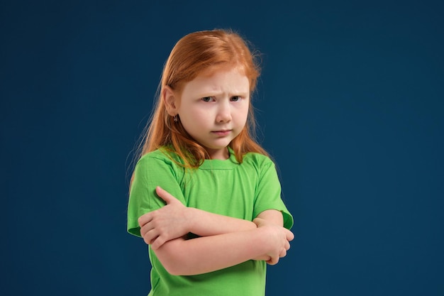 Cerrar foto de niña emocional pelirroja posando ante la cámara sobre fondo azul