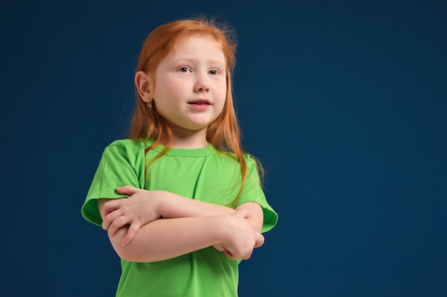 Cerrar foto de niña emocional pelirroja posando ante la cámara sobre fondo azul