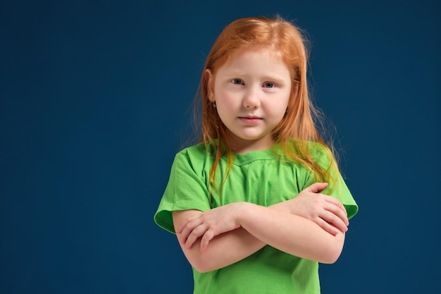 Cerrar foto de niña emocional pelirroja posando ante la cámara sobre fondo azul