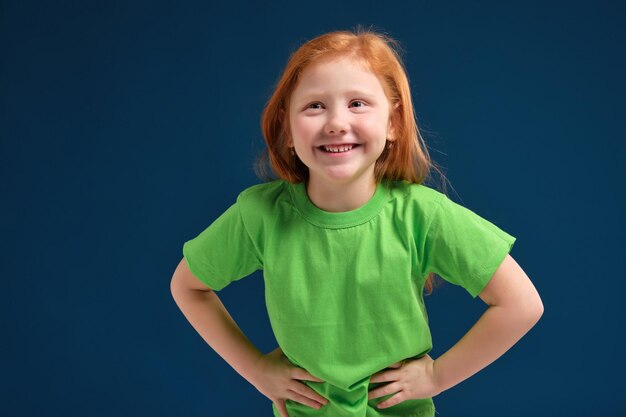 Cerrar foto de niña emocional pelirroja posando ante la cámara sobre fondo azul