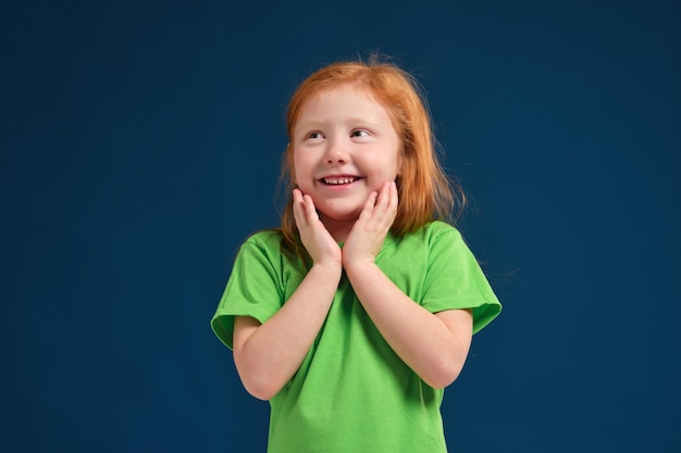 Cerrar foto de niña emocional pelirroja posando ante la cámara sobre fondo azul