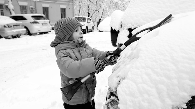 Cerrar foto de niño lindo feliz sonriente con abrigo beige y sombrero, divertirse jugando en la nieve en el invierno después de las nevadas