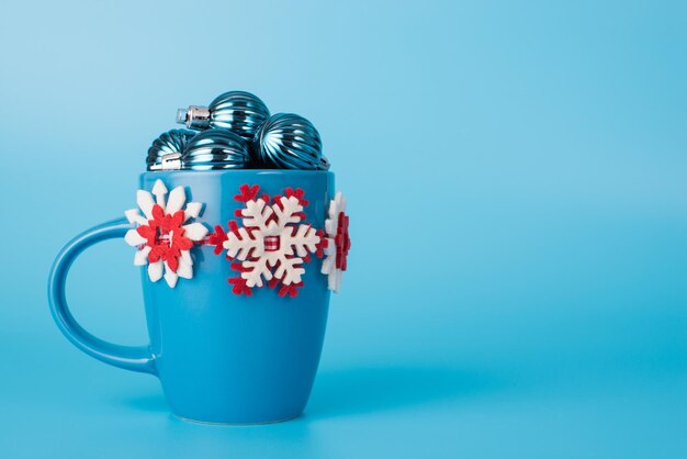 Cerrar foto de tamaño completo de taza creativa llena de pequeños adornos de árbol pequeño aislado sobre fondo azul de color pastel claro con copia espacio vacío en blanco