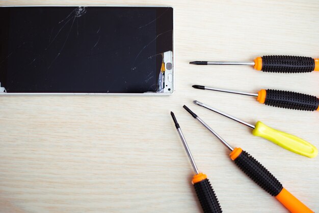 Cerrar foto de teléfono inteligente roto o dañado con herramientas profesionales sobre la mesa