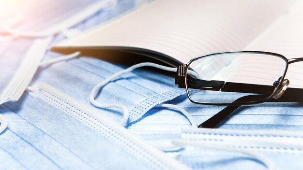 Cerrar imagen de cuaderno de máscaras faciales azules y gafas en el escritorio