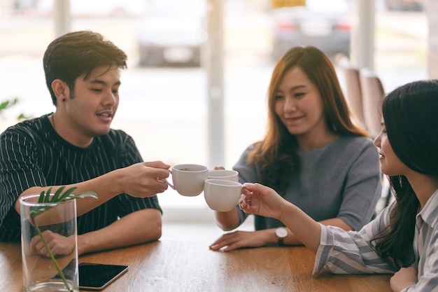 Cerrar imagen de tres asiáticos disfrutaron bebiendo y tintineando tazas de café en la mesa de madera en el café