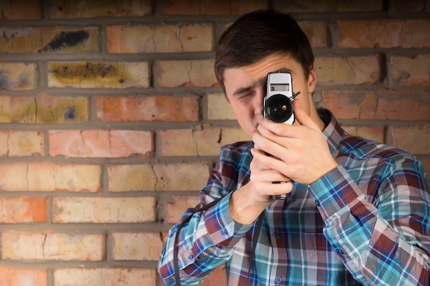 Foto cerrar joven en camisa a cuadros capturando algo con cámara portátil sobre un fondo de pared de ladrillo.