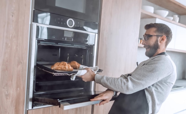 Cerrar un joven saca de la bandeja del horno de croissants