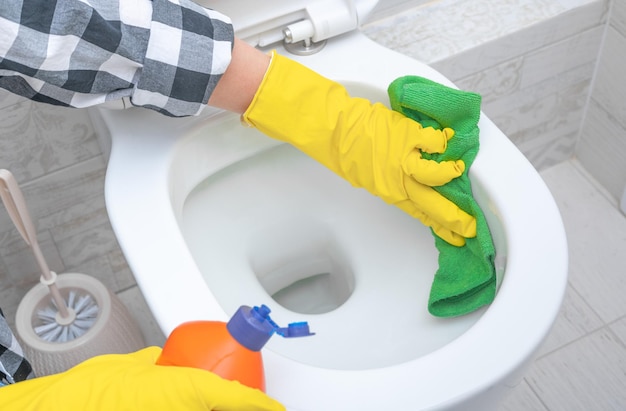 Cerrar la mano con detergente limpiando la taza del inodoro en el baño Hombre con guantes de goma amarillos limpiando el asiento del inodoro con un paño verde Higiene en el baño y el inodoro Limpieza de manos en la taza del inodoro en el baño