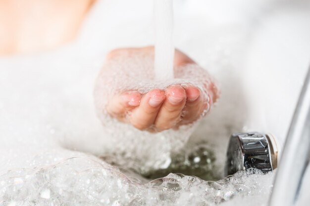 Cerrar la mano femenina en espuma jabonosa se sustituyó bajo el chorro de agua en el fregadero