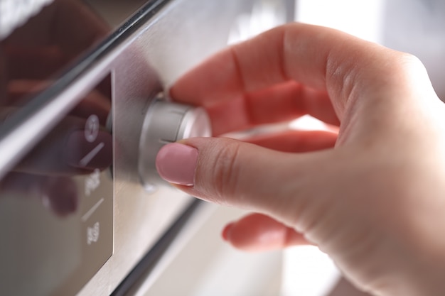 Cerrar una mano femenina mientras usa el microondas en su cocina