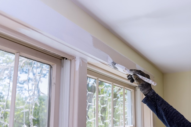 Cerrar la mano de un hombre en la pintura de un marco de ventana con color blanco