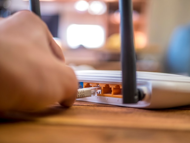 Cerrar una mano insertando el cable Ethernet en el enrutador wi-fi de la mesa de madera