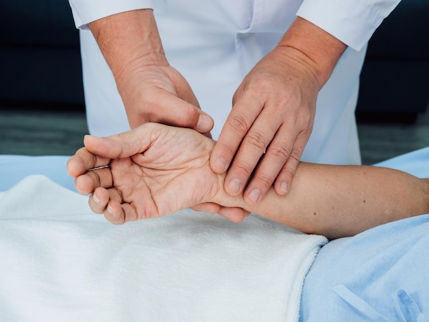 Cerrar la mano del médico con bata blanca de laboratorio sosteniendo la mano del paciente anciano que está acostado en la cama para comprobar el pulso del latido del corazón con los dedos en la sala de recuperación del hospital Concepto de control médico