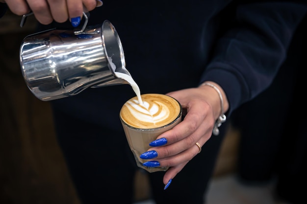 Cerrar la mano de una mujer barista vertiendo espuma de leche en café espresso
