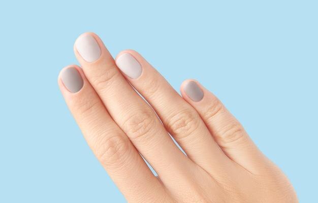 Cerrar la mano de una mujer con diseño de uñas gris sobre fondo azul