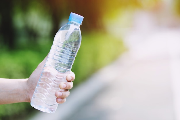 Cerrar la mano de la mujer joven sosteniendo una botella de agua potable fresca de un plástico en el parque.