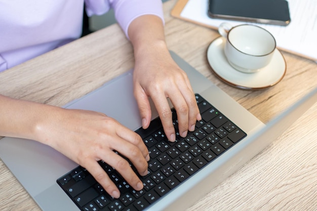 Cerrar la mano de una mujer de negocios escribiendo una computadora portátil con teclado en la oficina de escritorio