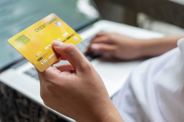 Cerrar mano de mujer con tarjeta de crédito y usando laptop