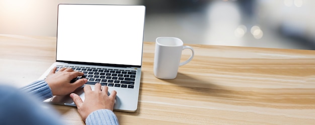 Cerrar la mano de la mujer trabajando y escribiendo en la computadora portátil en la mesa de madera, portátil de pantalla blanca para el proyecto actual y productos con tabla de espacio de copia