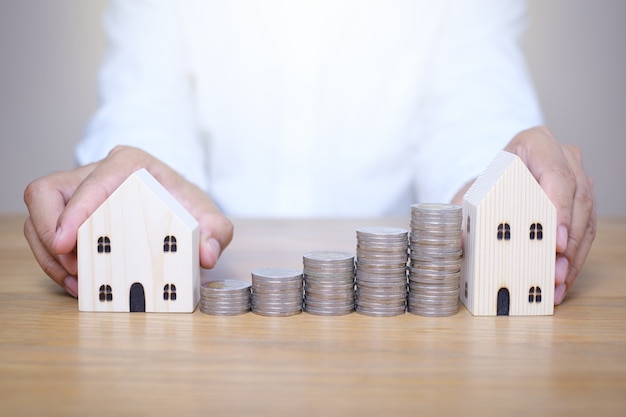 Foto cerrar mano poniendo pilas de monedas cerca del modelo de casa en la mesa de madera