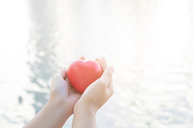 Cerrar mano sosteniendo corazón rojo sobre fondo suave de río y agua