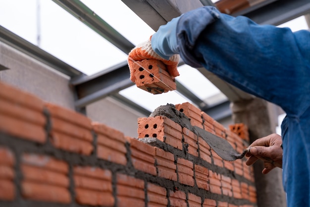 Cerrar la mano del trabajador albañil instalando mampostería de ladrillo en la pared exterior en el sitio de construcción