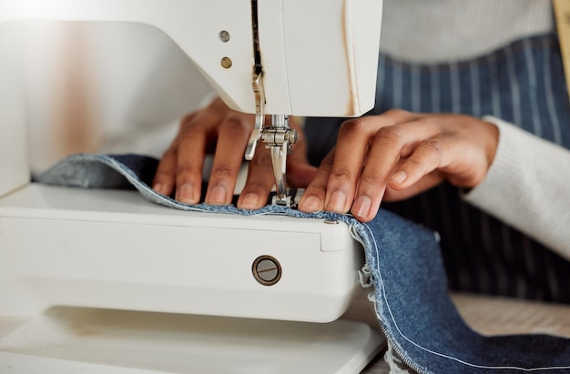 Cerrar las manos de una diseñadora profesional sentada en una máquina de coser en su estudio Proceso de un sastre en el trabajo de reparación y diseño de ropa Alteraciones casuales que se están haciendo a los jeans