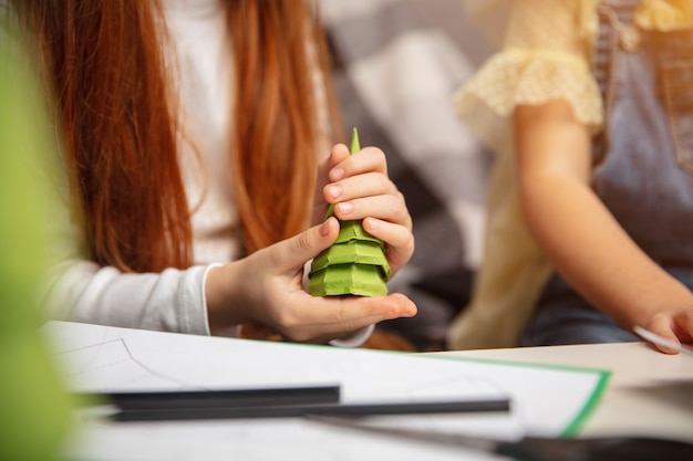 Cerrar las manos de dos niños pequeños, niñas juntas en la creatividad de la casa. Los niños hacen juguetes hechos a mano para juegos o celebración de Año Nuevo. Pequeños modelos caucásicos. Infancia feliz, Navidad.