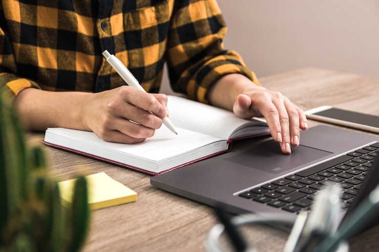 Foto cerrar las manos de una empresaria, estudiante o profesional independiente en camisa amarilla haciendo notas en su cuaderno. el estudio es poder