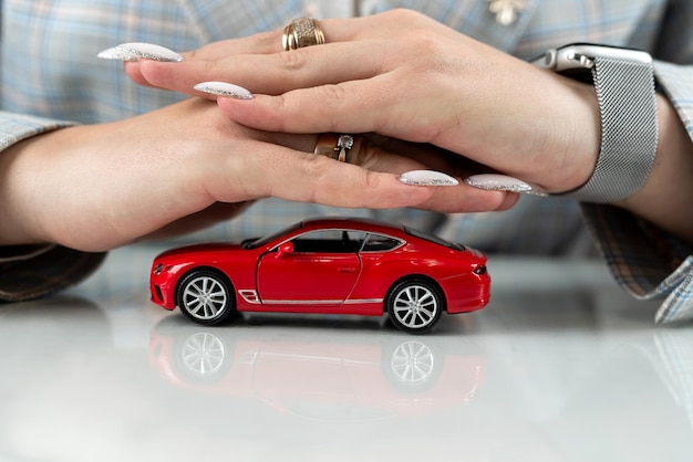 Foto cerrar las manos femeninas con coche de juguete rojo como concepto de protección de seguro