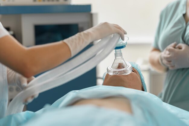 Cerrar las manos del médico anestesiólogo que sostiene la máscara de respiración en la cara del paciente durante la operación