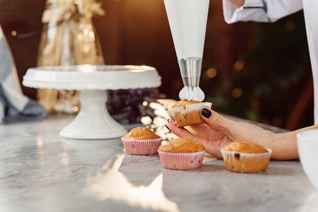 Cerrar las manos de la mujer chef con bolsa de confitería exprimiendo crema en cupcakes.