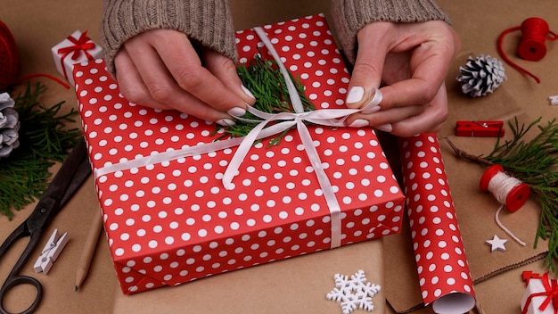 Cerrar las manos de la mujer de embalaje y envoltura de cajas de regalo de Navidad con papel rojo, vista de ángulo alta