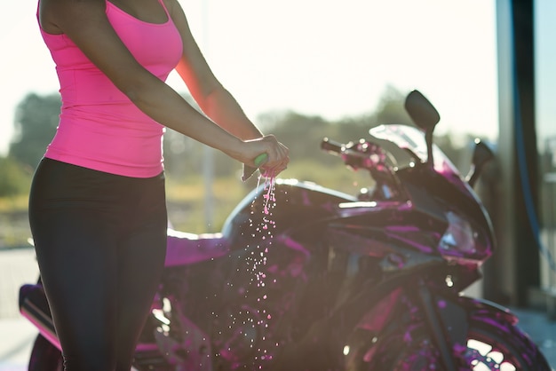 Cerrar las manos de la mujer exprime la humedad del trapo mientras limpia la motocicleta deportiva en autoservicio