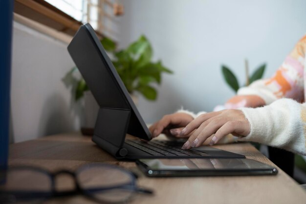 Cerrar manos de mujer joven escribiendo en el teclado inalámbrico de la tableta digital